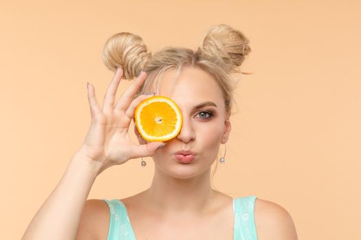Pretty charming joyful attractive cheerful funny comic positive nude natural pure girl having two pieces of orange, closing one eye, isolated on beige background with copy space for advertisement