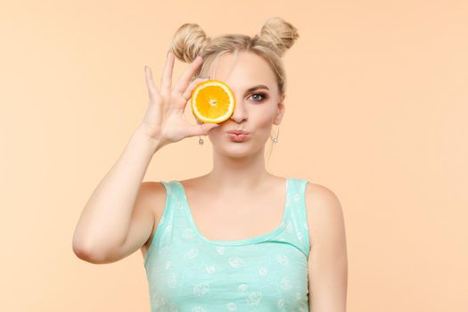Pretty charming joyful attractive cheerful funny comic positive nude natural pure girl having two pieces of orange, closing one eye, isolated on beige background with copy space for advertisement