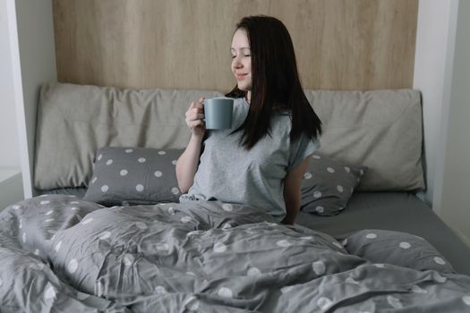 morning, coziness, cozy home concept - a young woman with cup of coffee or cacao in bed at home.