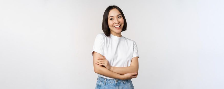 Portrait of happy asian woman smiling, posing confident, cross arms on chest, standing against studio background.