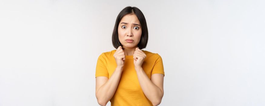 Portrait of scared asian woman shaking from fear, looking terrified and concerned, standing anxious against white background.