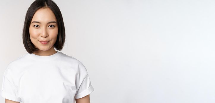 Close up portrait of young asian woman looking at camera, wearing t-shirt, smiling and looking happy, white background.