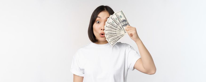 Happy asian girl holding money, cash near face, concept of microcredit and finance, white studio background. Copy space