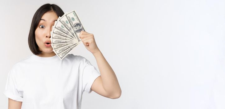 Happy asian girl holding money, cash near face, concept of microcredit and finance, white studio background. Copy space