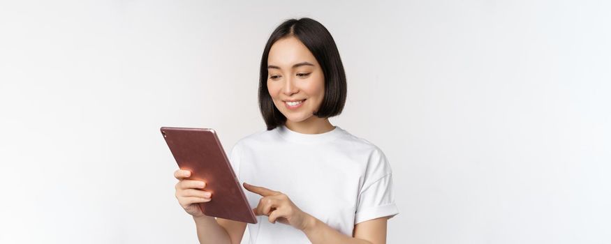 Asian girl using digital tablet, working with gadget, shopping online, standing over white background.