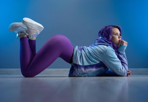 girl in stylish purple sportswear and with purple hair is sexy lying on the floor