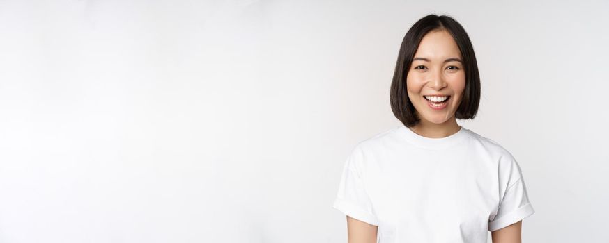 Close up portrait of young asian woman looking at camera, wearing t-shirt, smiling and looking happy, white background.