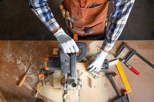 Top view of carpenter holding plank near circular saw in carpentry shop. High quality photo.