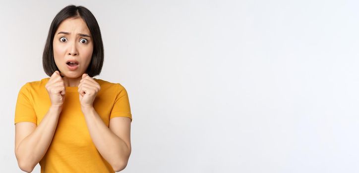 Portrait of scared asian woman shaking from fear, looking terrified and concerned, standing anxious against white background.