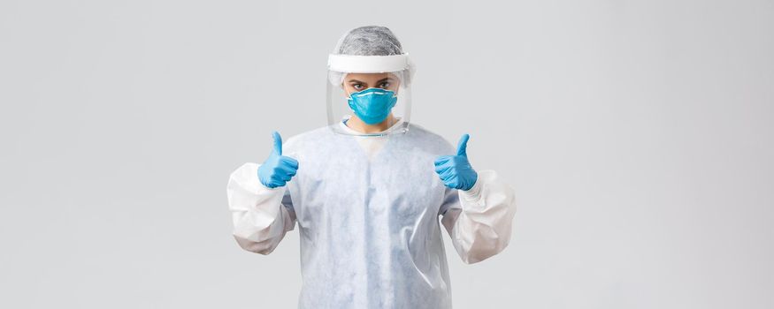 Covid-19, preventing virus, health, healthcare workers and quarantine concept. Determined confident doctor, nurse in personal protective equipment, respirator and gloves, show thumbs-up, fight corona.