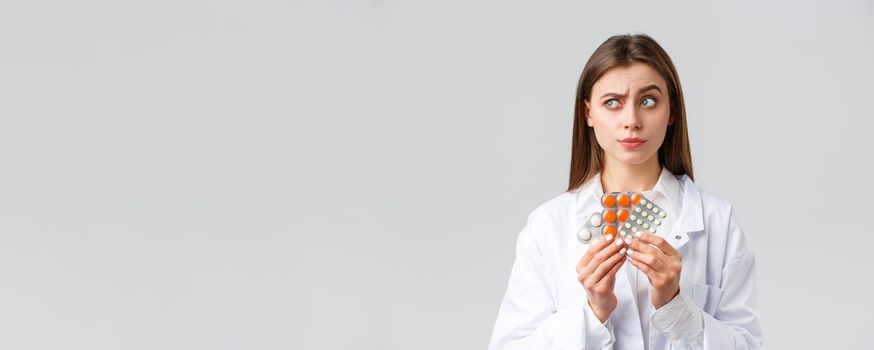 Pharmacy, healthcare workers, insurance and hospitals concept. Thoughtful and skeptical female doctor in white scrubs, look away thinking, consider what pills needed, show medicine.