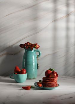 still life with pink strawberry pancakes on a turquoise plate with sour cream and fresh strawberries, cultural exotic food, creative breakfast for Valentine's holiday against a turquoise vase