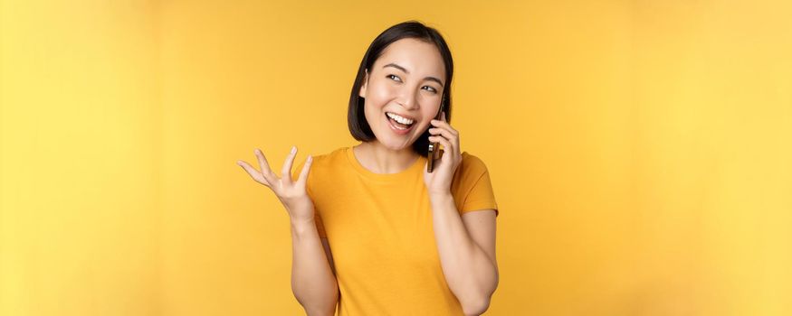 Young korean girl talking on mobile phone. Asian woman calling on smartphone, standing over yellow background.