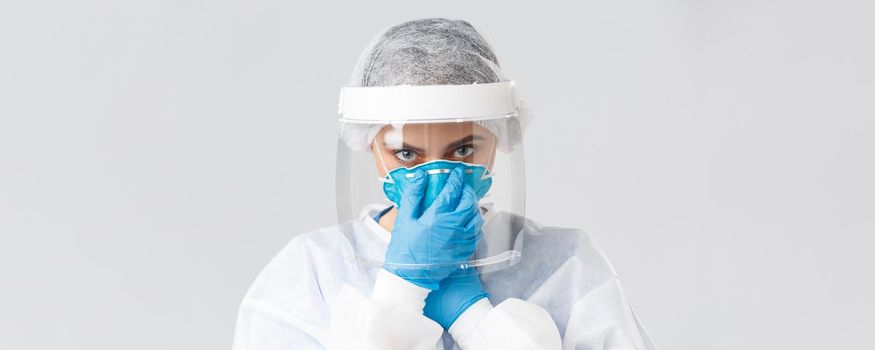 Covid-19, preventing virus, health, healthcare workers and quarantine concept. Close-up serious female doctor, nurse in personal protective equipment, put on respirator, look camera determined.