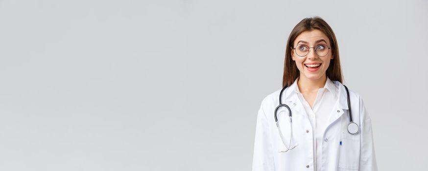 Healthcare workers, medicine, insurance and covid-19 pandemic concept. Happy optimistic female doctor, physician with stethoscope in white scrubs and glasses, look upper left corner with upbeat smile.