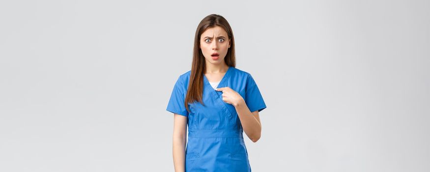 Healthcare workers, prevent virus, insurance and medicine concept. Confused and shocked female nurse in scrubs pointing at herself, gasping surprised, cant believe, being chosen or accused.