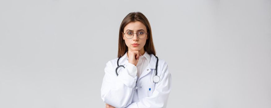 Healthcare workers, medicine, insurance and covid-19 pandemic concept. Serious smart, professional female doctor in glasses and white scrubs, thinking, taking decision or choice, look camera.