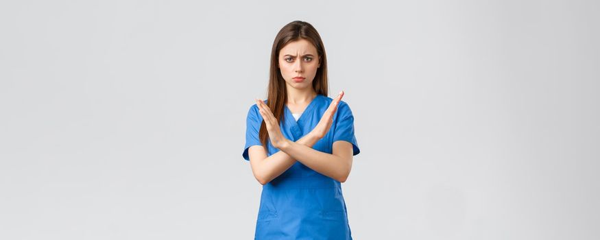 Healthcare workers, prevent virus, insurance and medicine concept. Angry serious-looking nurse, doctor in blue scrubs cross hands in stop sign, prohibit or forbid action, frowning displeased.