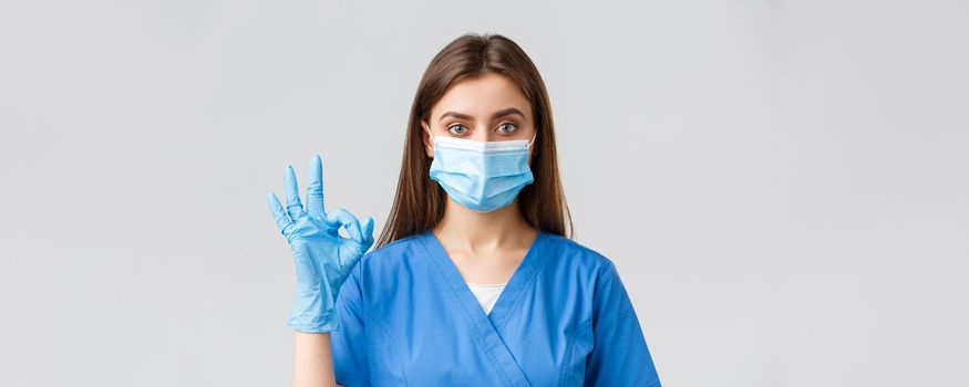 Covid-19, preventing virus, health, healthcare workers and quarantine concept. Confident female nurse or doctor working in clinic with coronavirus patients, in medical mask, show okay sign.