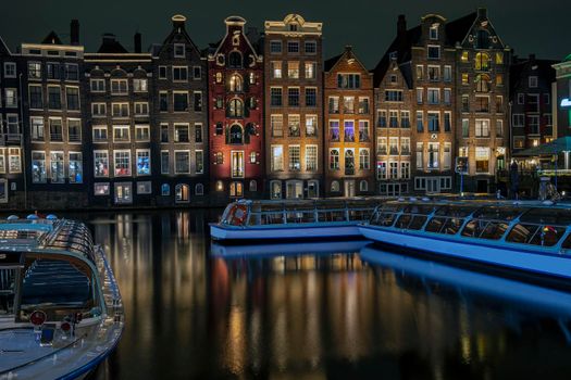Traditonal houses and cruise boats at the Damrak in Amsterdam in the Netherlands by night