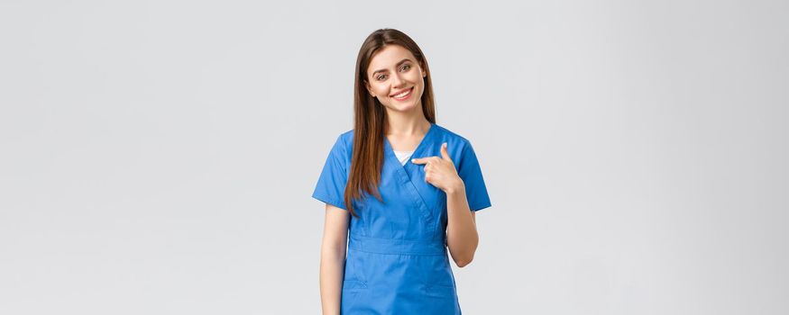 Healthcare workers, prevent virus, insurance and medicine concept. Pleasant smiling pretty nurse, female doctor in blue scrubs, pointing herself, ready help, saving patients.