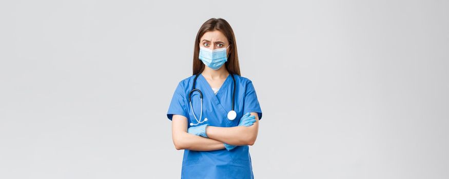 Covid-19, preventing virus, health, healthcare workers and quarantine concept. Skeptical and concerned female nurse in blue scrubs, stethoscope and personal protective equipment look suspicious.