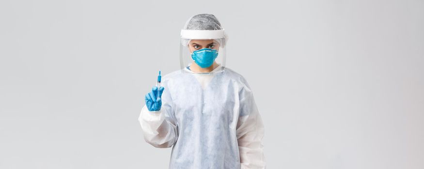 Covid-19, medical research, diagnosis, healthcare workers and quarantine concept. Serious doctor or nurse in personal protective equipment, face shield holding syringe with coronavirus vaccine.