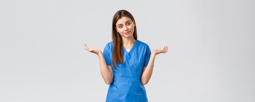 Healthcare workers, prevent virus, insurance and medicine concept. Doctor shrugging as cant tell, have no idea, sorry dont know. Female nurse in blue scrubs spread hands sideways.