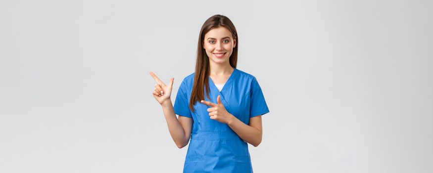 Healthcare workers, prevent virus, insurance and medicine concept. Professional smiling, attractive female nurse or doctor in blue scrubs, physician pointing finger left at banner, recommend clinic.