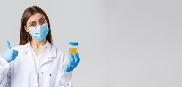 Covid-19, medical research, diagnosis, healthcare workers and quarantine concept. Doctor or clinic lab employee holding patient urine sample, wear medical mask and gloves, thumb-up.