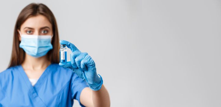 Covid-19, preventing virus, health, healthcare workers and quarantine concept. Close-up of serious-looking young doctor or nurse in clinic, lab showing coronavirus vaccine in ampoule.