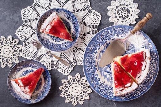 Christmas red strawberry pie on blue plates and a gift in a red box on the table, flat lay colorful food on white knitted napkins in the form of snowflakes, winter mood. High quality photo