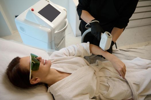 Overhead view of a beautiful Caucasian woman receiving a hair removal procedure in a wellness spa clinic. Hardware cosmetology, beauty treatment and body care concept