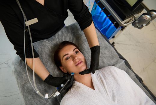 Beautiful Caucasian woman lying on a massage table and getting a hydro microdermabrasion facial treatment for skin rejuvenation. Hardware cosmetology, anti-aging therapy, rejuvenation