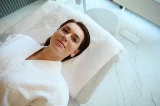 Overhead view of a beautiful woman with perfect glowing skin lying down on a massage table in a spa room, relaxing while receiving a professional skin and body care treatment in wellness spa clinic