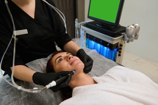 Beautiful Caucasian woman getting facial hydro microdermabrasion peeling treatment at spa center. Hydra Vacuum Cleaner. Exfoliation, Rejuvenation And Hydration.