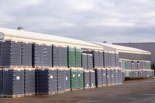 Outdoors warehouse with packages of brown and green bottles for bottling beer on the territory of the brewery. The bottles are packed on pallets and covered with plastic.