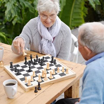 An elderly couple playing chess together outdoors.