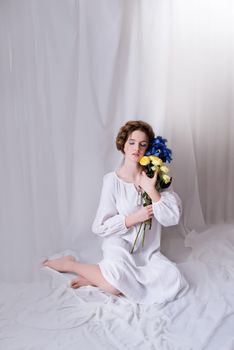 Caucasian Ukrainian teenager sitting in the studio in a dress and ellow-blue flowers on a white background during the war. Calm lady is sleeping. Concept - Stop the war in Ukraine.