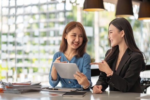 Two young asian businesswoman talking discussion in group meeting at office table in a modern office interior. Business collaboration strategic planning and brainstorming of coworkers.