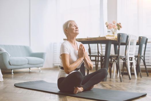 elderly woman meditating sitting on the floor in her living room. concept of a healthy lifestyle.