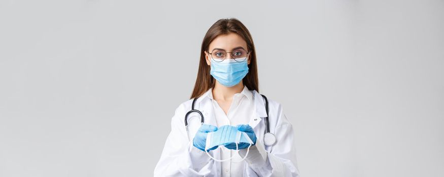 Covid-19, preventing virus, clinic, healthcare workers and quarantine concept. Young doctor in medical mask and gloves, white scrubs, giving face mask protection to patients, look serious.