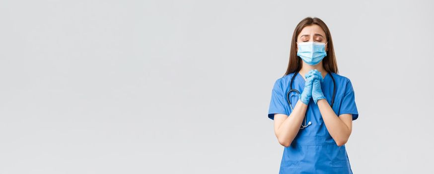 Covid-19, preventing virus, health, healthcare workers and quarantine concept. Hopeful female nurse or doctor in blue scrubs, medical mask, praying for lives of patients sick coronavirus infection.