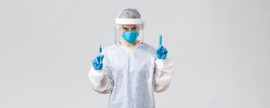 Covid-19, medical research, diagnosis, healthcare workers and quarantine concept. Determined doctor in PPE costume, personal protective equipment, hold syringe with coronavirus vaccine for patient.