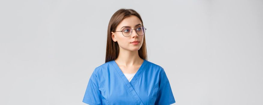 Healthcare workers, medicine, insurance and covid-19 pandemic concept. Thoughtful pretty professional female nurse, doctor in glasses and scrubs, looking right curious, thinking, observe something.