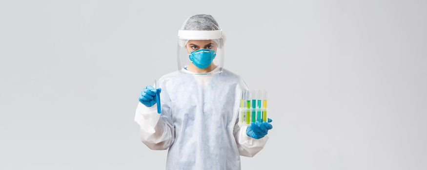 Covid-19, medical research, diagnosis, healthcare workers and quarantine concept. Doctor in personal protective equipment hold test-tubes with coronavirus vaccines, working in clinic laboratory.