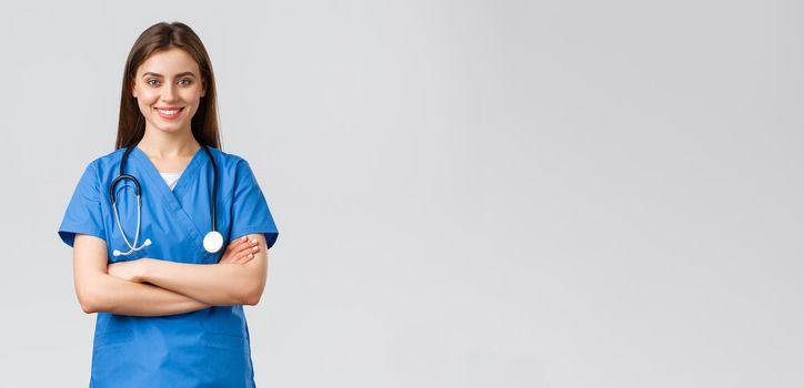 Medical workers, healthcare, covid-19 and vaccination concept. Optimistic confident, professional female nurse or doctor in blue scrubs with stethoscope, cross arms chest and smiling optimistic.