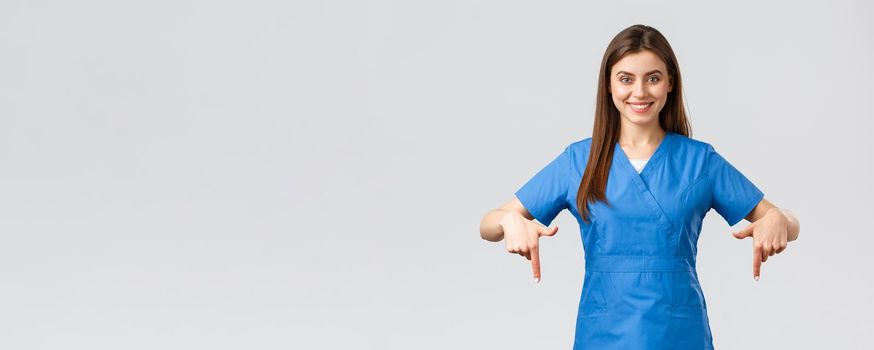 Healthcare workers, prevent virus, covid-19 test screening, medicine concept. Smiling confident nurse, doctor or intern in blue scrubs, pointing fingers down as give patients information.