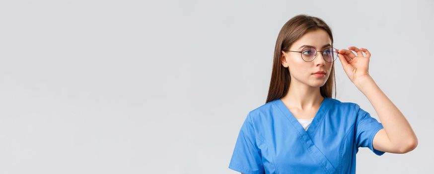 Healthcare workers, medicine, insurance and covid-19 pandemic concept. Professional young smart doctor or nurse, female intern in scrubs and glasses, looking right at banner serious face.