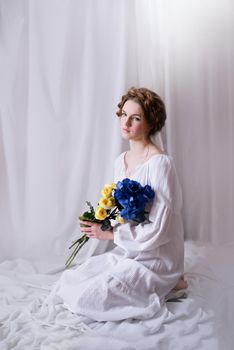 Caucasian Ukrainian woman sitting in the studio in a dress and yellow-blue flowers on a white background during the war. Concept - Stop the war in Ukraine.